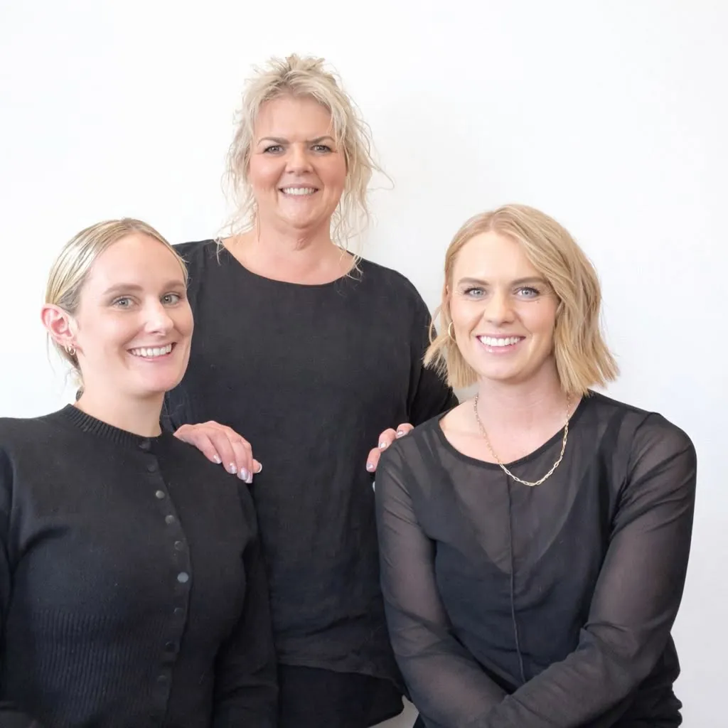 Brooke, Leanne and Olivia from Unique Hair and Beauty, smiling together in black against a white wall